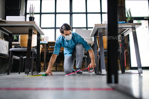 Portrait of young businessman with face mask working indoors in office, marking safe distance.