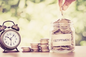 putting coins in glass jar with retro alarm clock for time to money saving for retirement concept