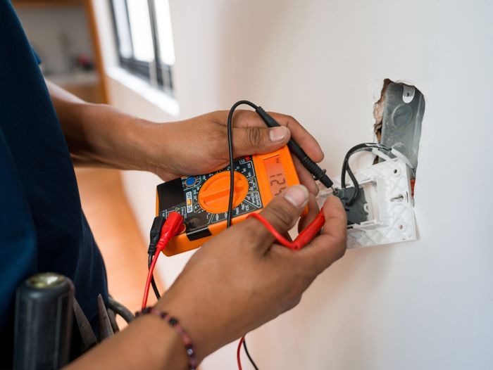 Close-up on an electrician fixing an electrical outlet and measuring the voltage using a multimeter