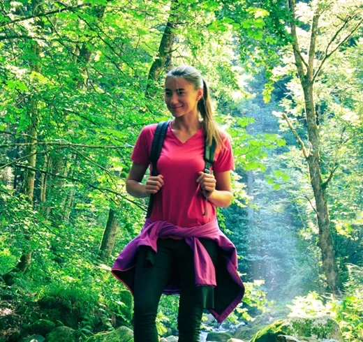 Woman hiking in pink shirt with backpack and jacket tied around waist