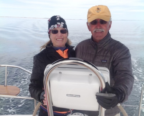 Captain Waddell sailing on a calm sea, smiling at the helm of their boat under a clear sky.