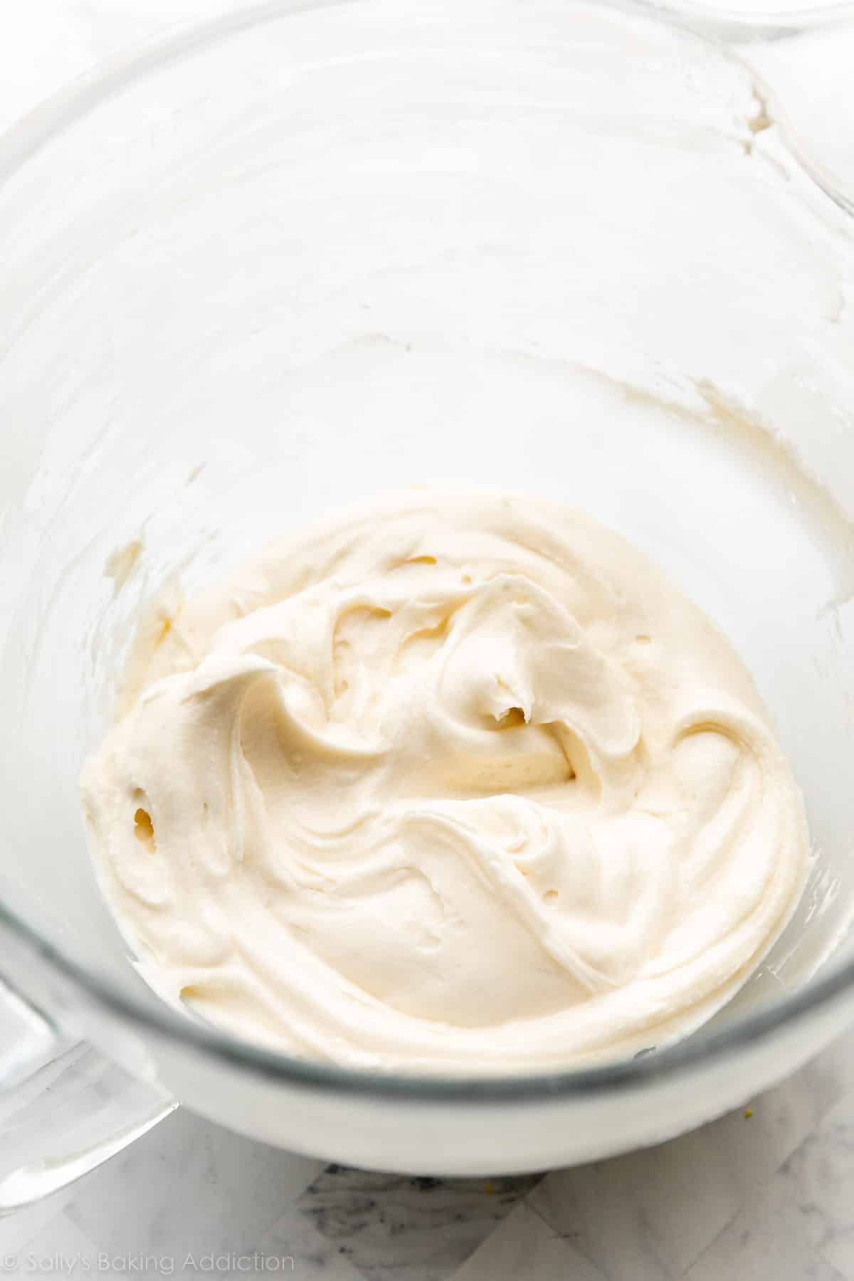 creamy cheese frosting in glass bowl on marble countertop.