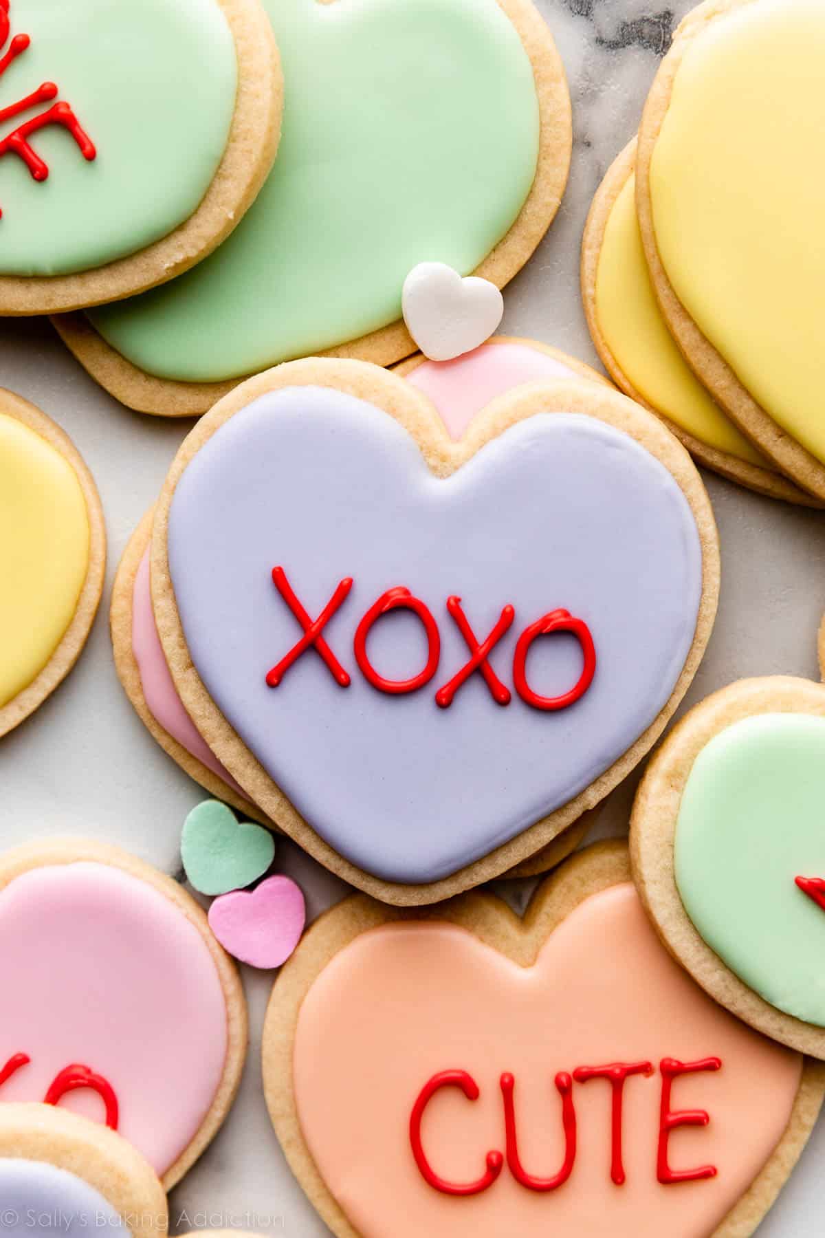 heart-shaped Valentine's Day cookies with pastel royal icing and red writing to look like conversation heart candies.