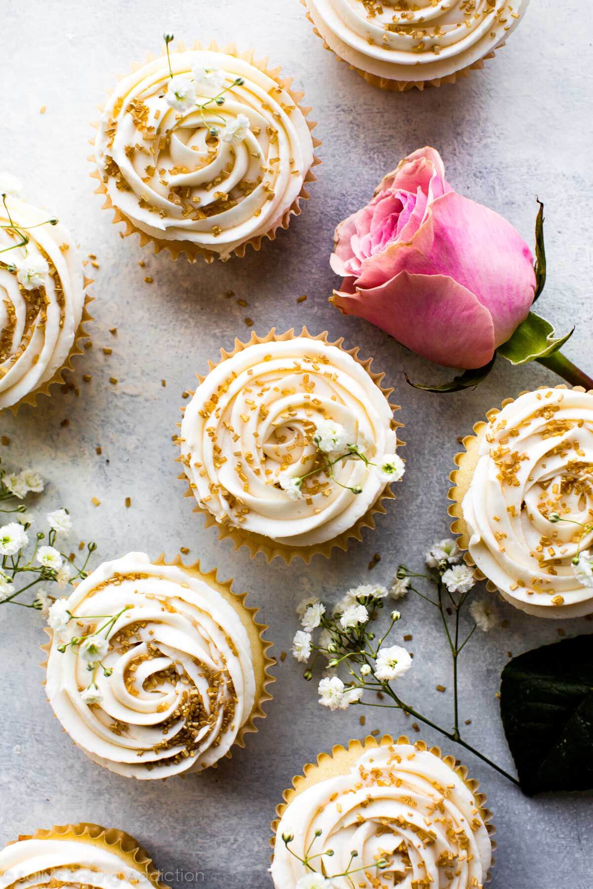 overhead image of vanilla wedding cupcakes topped with champagne frosting and gold sprinkles