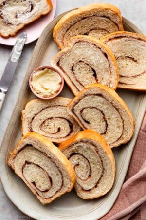 slices of homemade cinnamon swirl yeasted bread slices on gray platter with pink dish of butter.