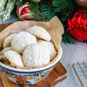 Snowball cookies in a bowl with Christmas decorations in the background.