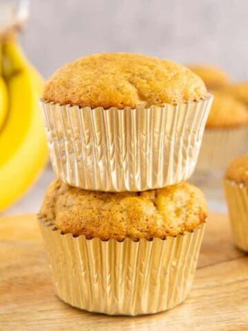 Two banana bread muffins stacked on top of each other with bananas in the background.