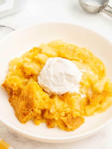 3 ingredient pineapple dump cake served in a white bowl with a scoop of coconut icecream.