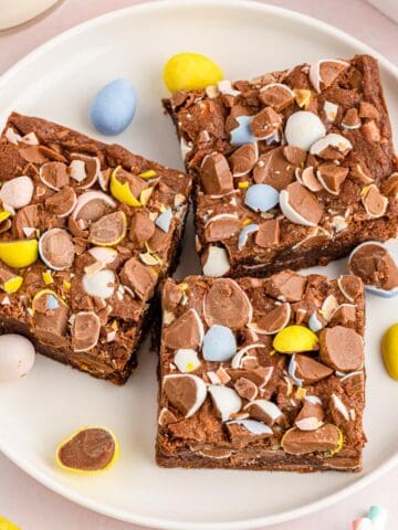 Mini egg brownies served on a white plate with more mini eggs scattered around.