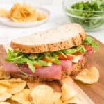 A ploughman's sandwich with kettle cooked chips on a wooden board.