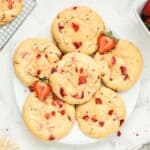 Strawberry cheesecake cookies stacked on a white plate and garnished with fresh strawberries.