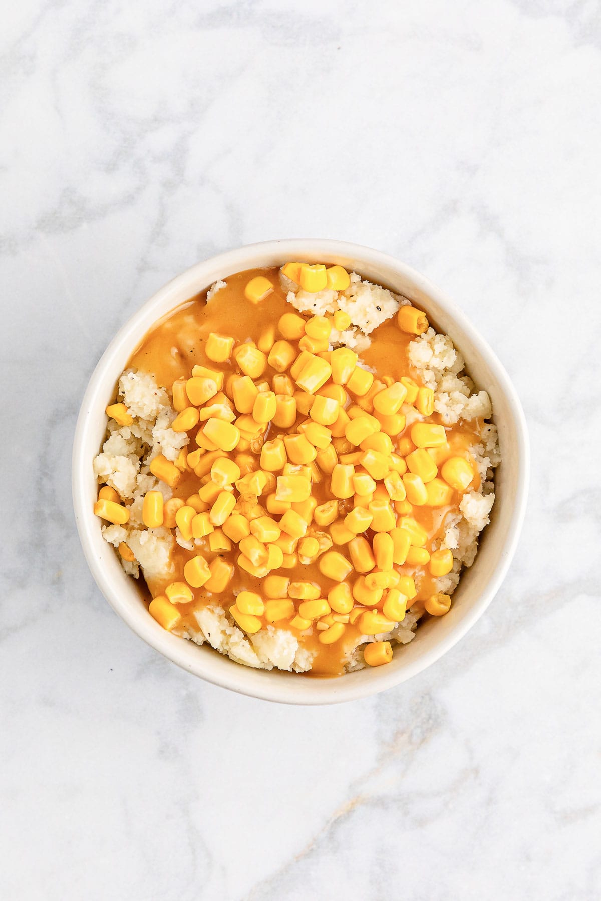 Adding gravy and corn kernels to make a copycat KFC famous bowl.