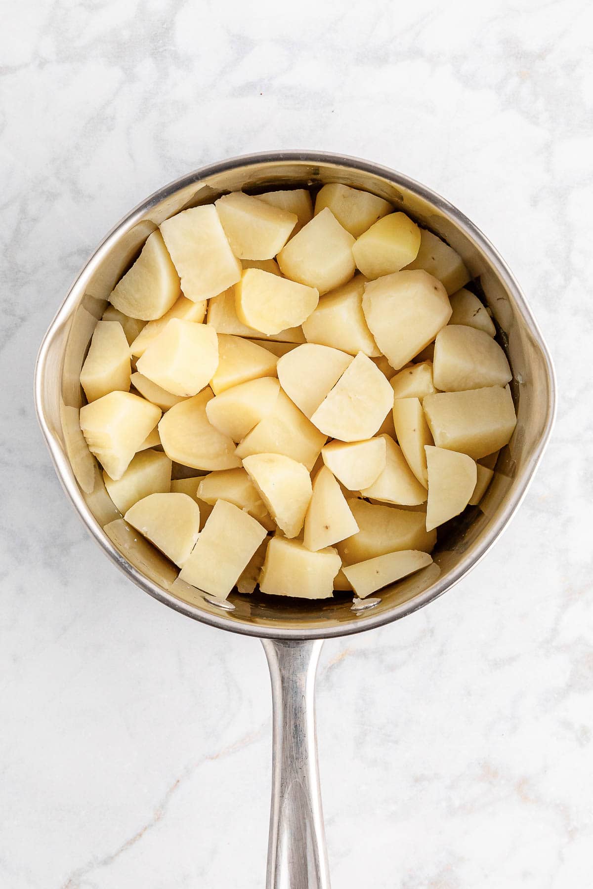 Peeled and diced potatoes in a stainless steel saucepan, ready to make mashed potatoes.