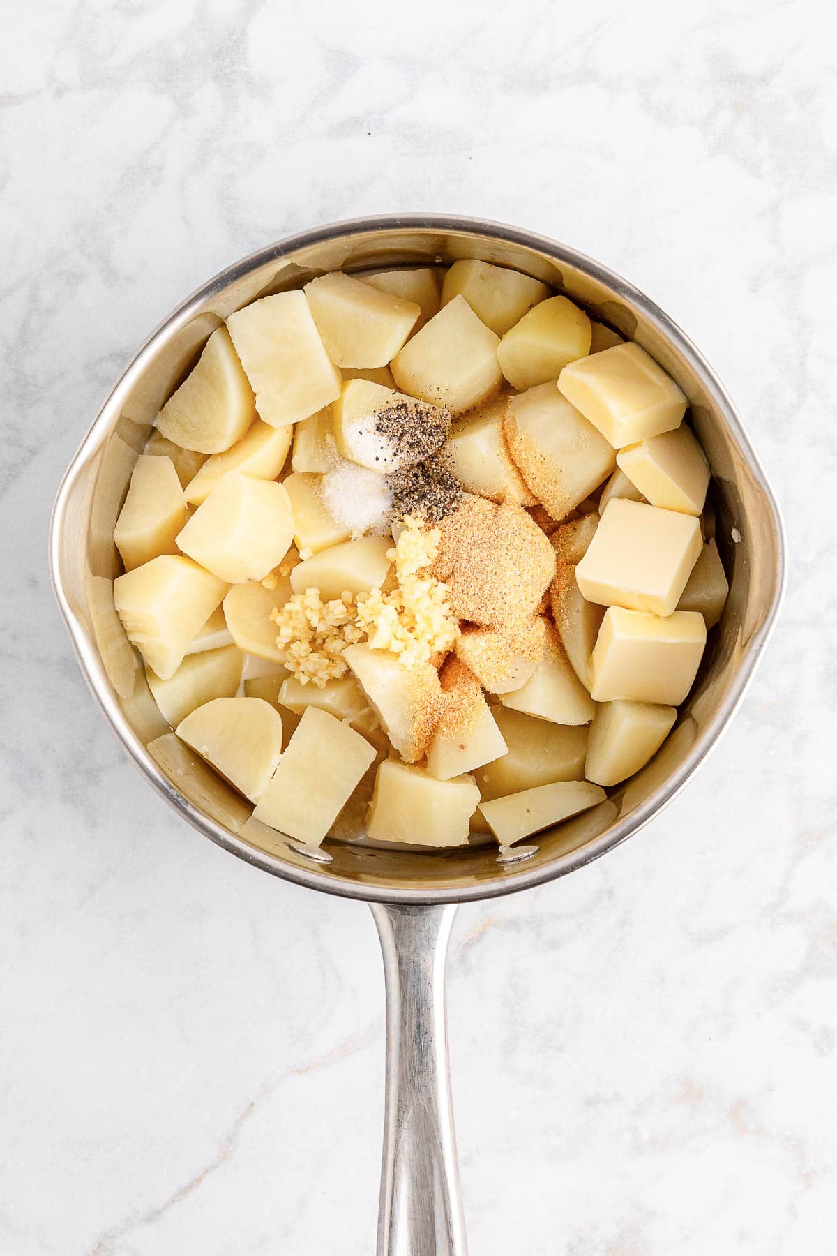 Adding salt, pepper, and garlic to potatoes to make mashed potatoes.