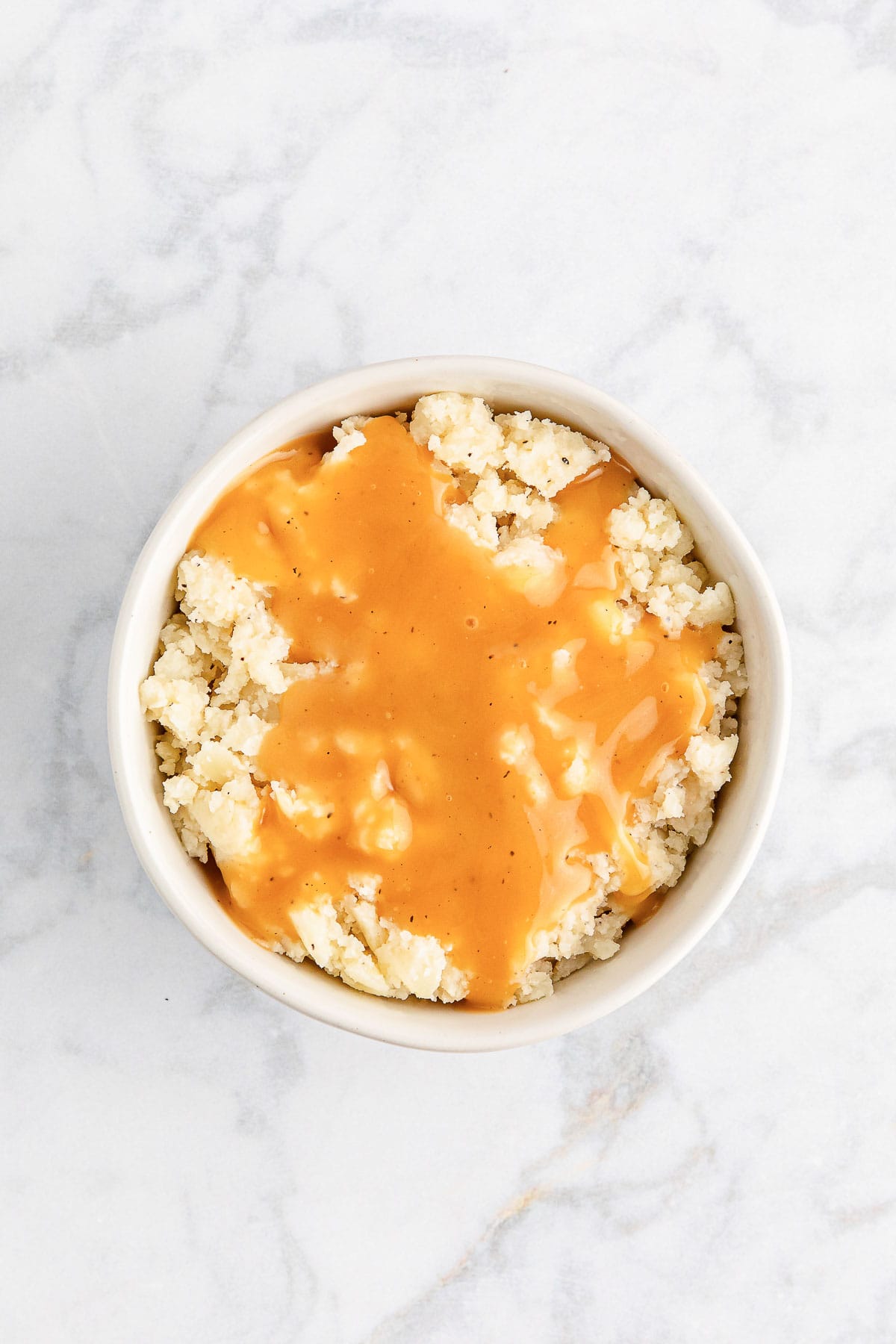 Pouring gravy over mashed potatoes to make a homemade KFC famous bowl.