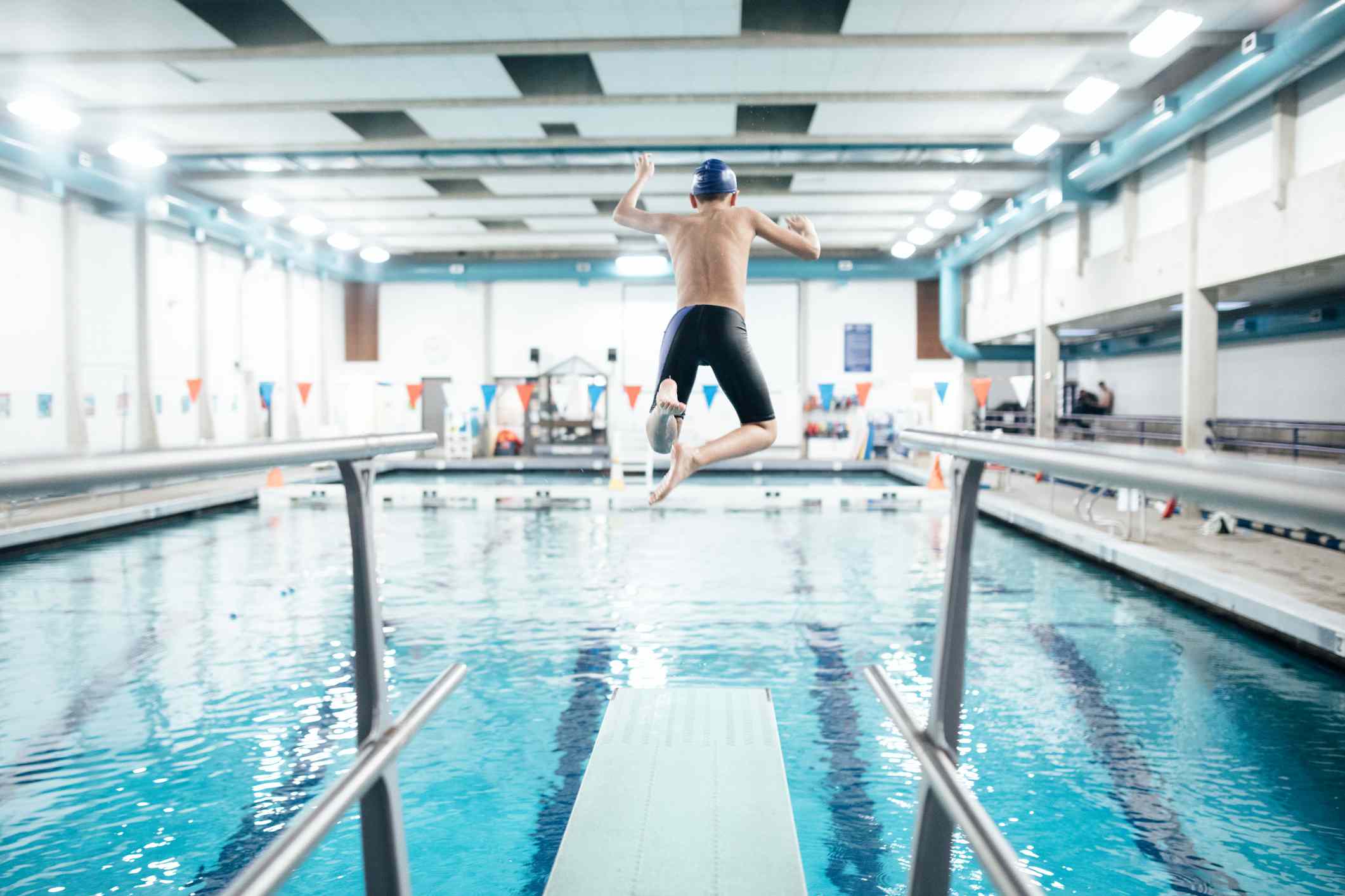 Boy jumping off a diving board into an indoor pool