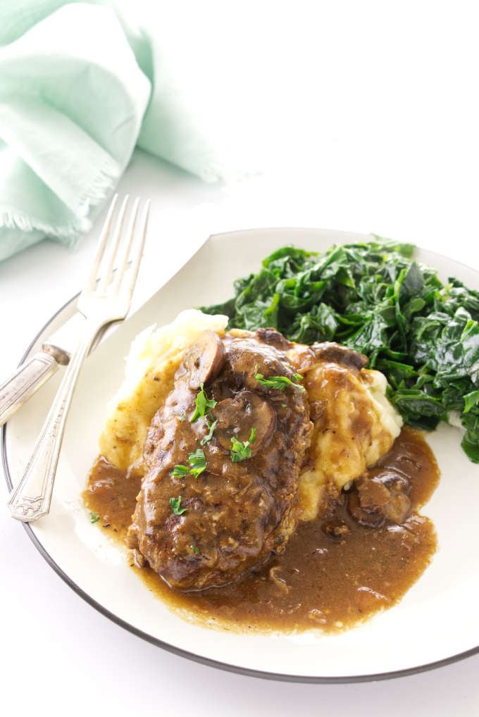 Serving of salisbury steak on mashed potatoes with a side of sauteed greens