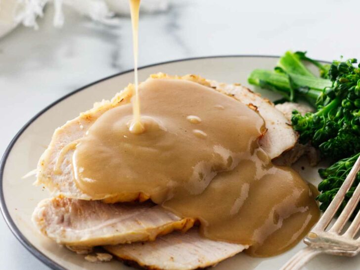 Drizzling gravy over slices of turkey on a plate.