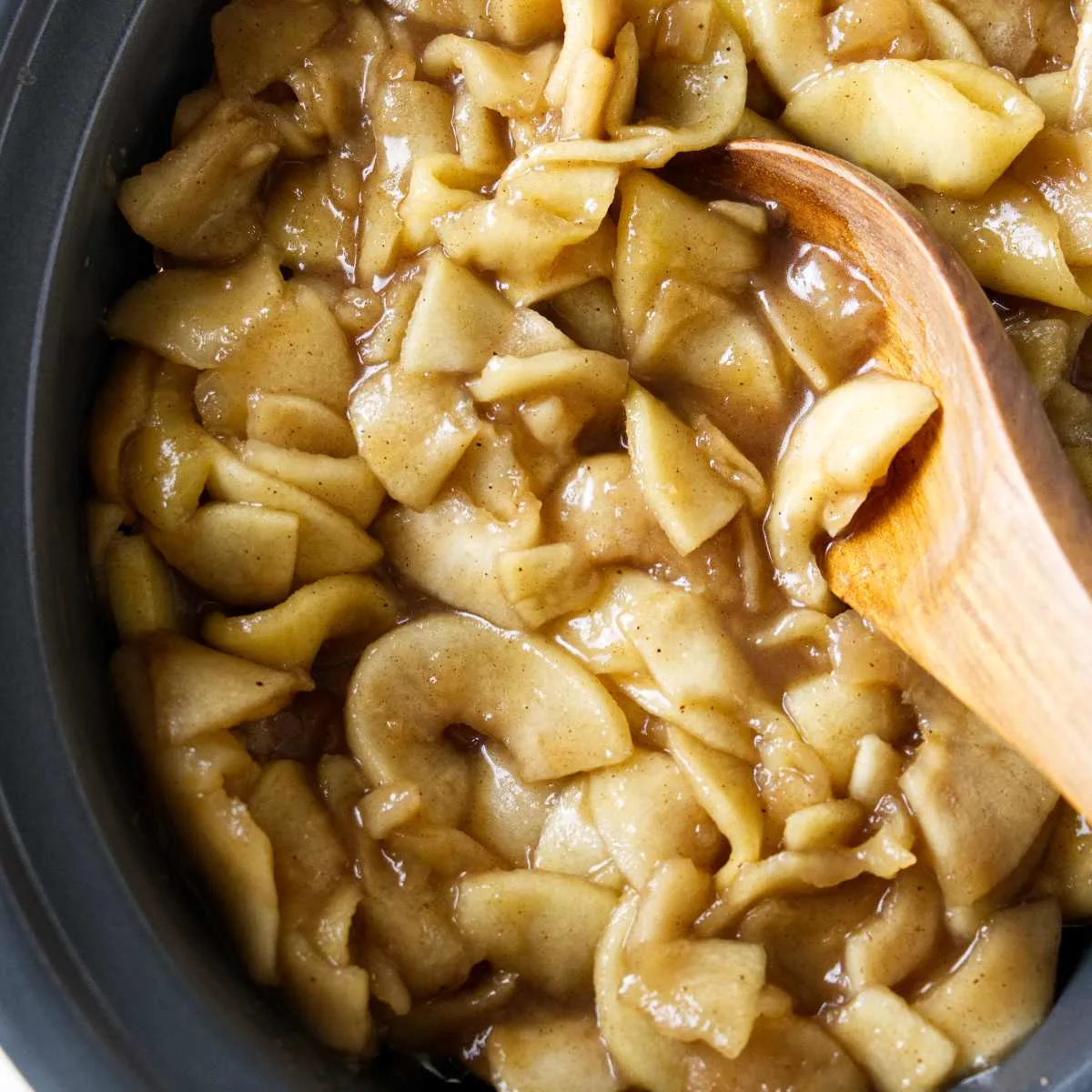 Scoopping homemade apple pie filling out of a crock pot.