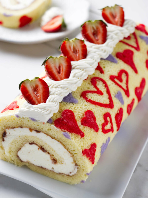 A valentine cake strawberry cake roll on a serving platter.