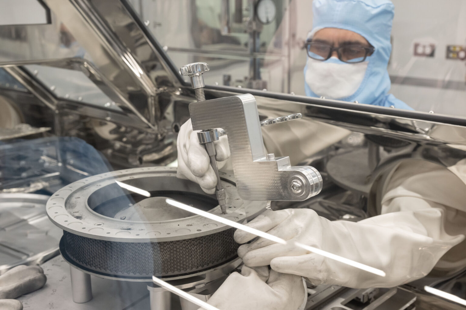 Person in cleanroom suit attached a tool to the TAGSAM from outside of the protective barrier