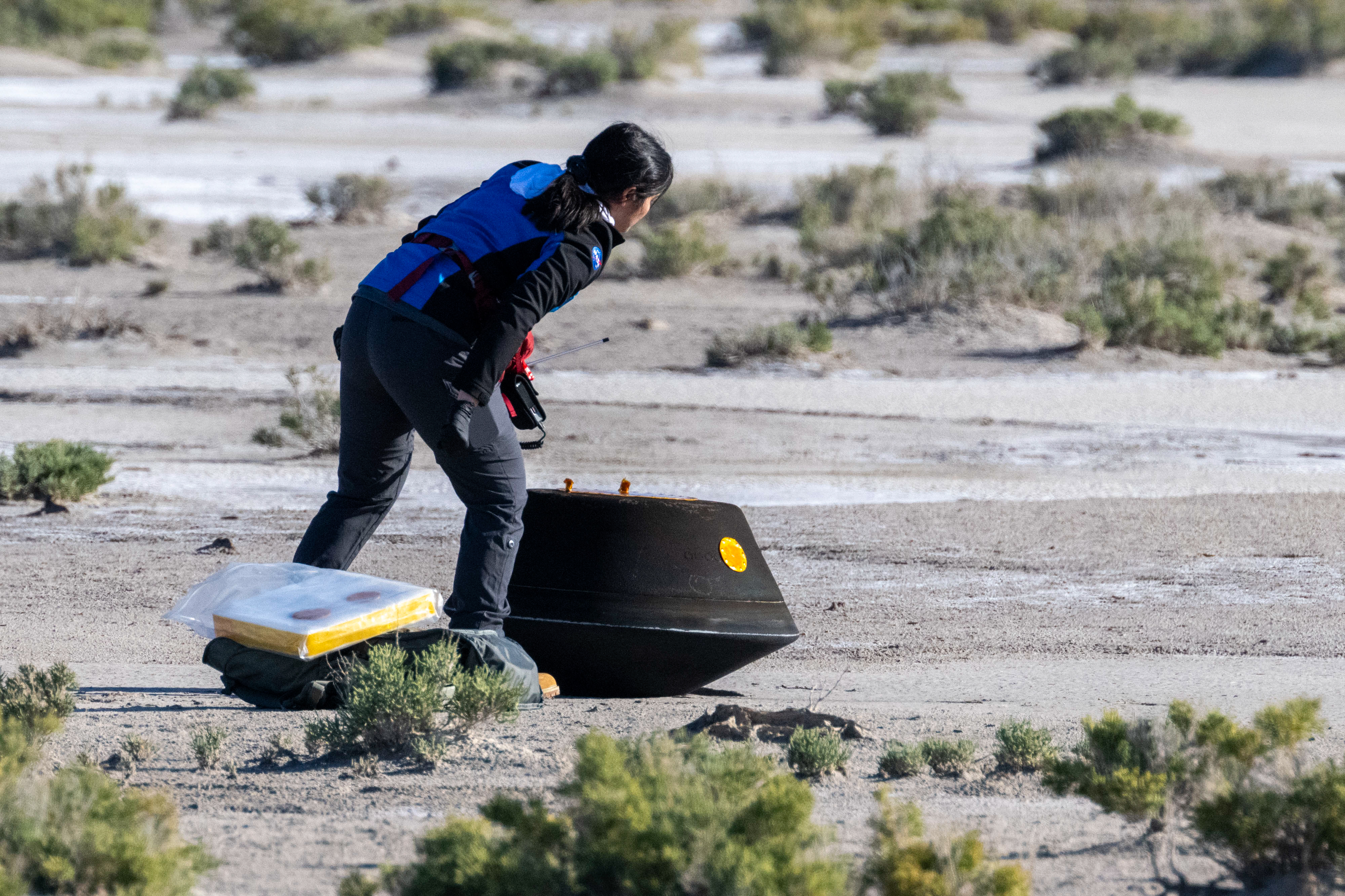 A woman wearing a blue jacket and black pants examines the capsule.⁣