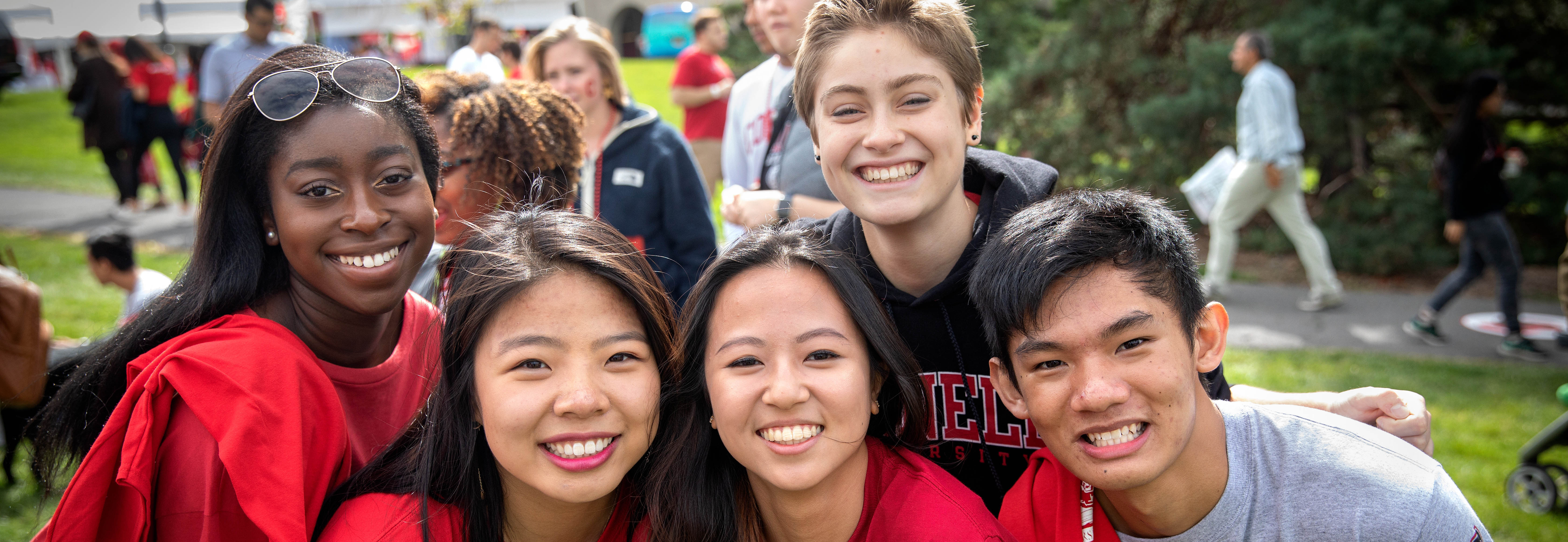 Five students posing outside of Schoellkopf Field in Cornell red clothing