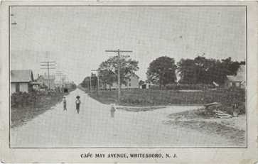 Black and white photograph of three children walking down street.  There are houses in the background.