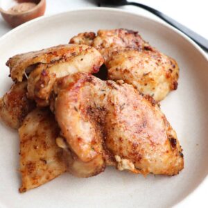 finished ninja foodi chicken thighs on a cream plate with seasoning in the background