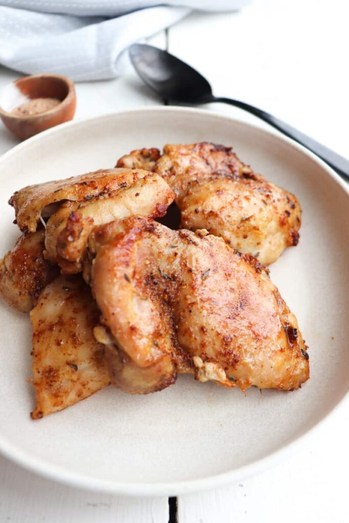 finished ninja foodi chicken thighs on a cream plate with seasoning in the background