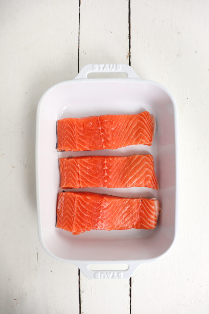 3 salmon filets lined up in a white dish.