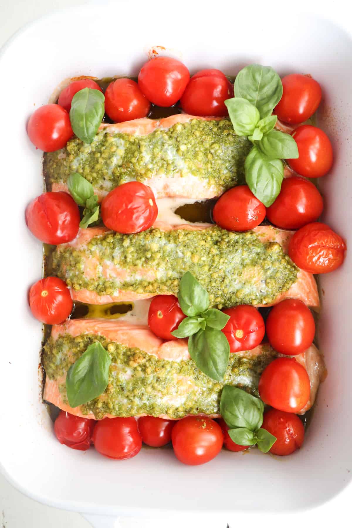 finished pesto butter salmon with tomatoes garnished with basil.