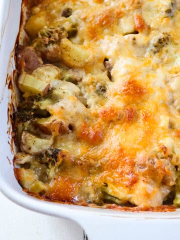 up close on finished chicken potato broccoli casserole in a white baking dish.