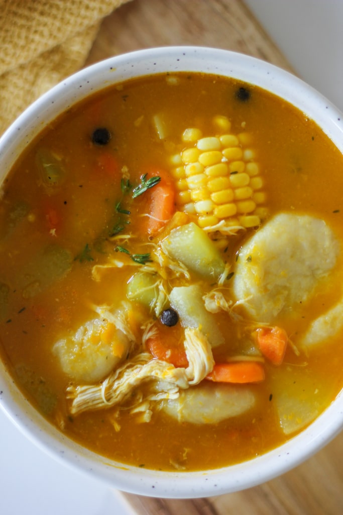 chicken soup in white bowl with corn, dumpling, chicken, and veggies.