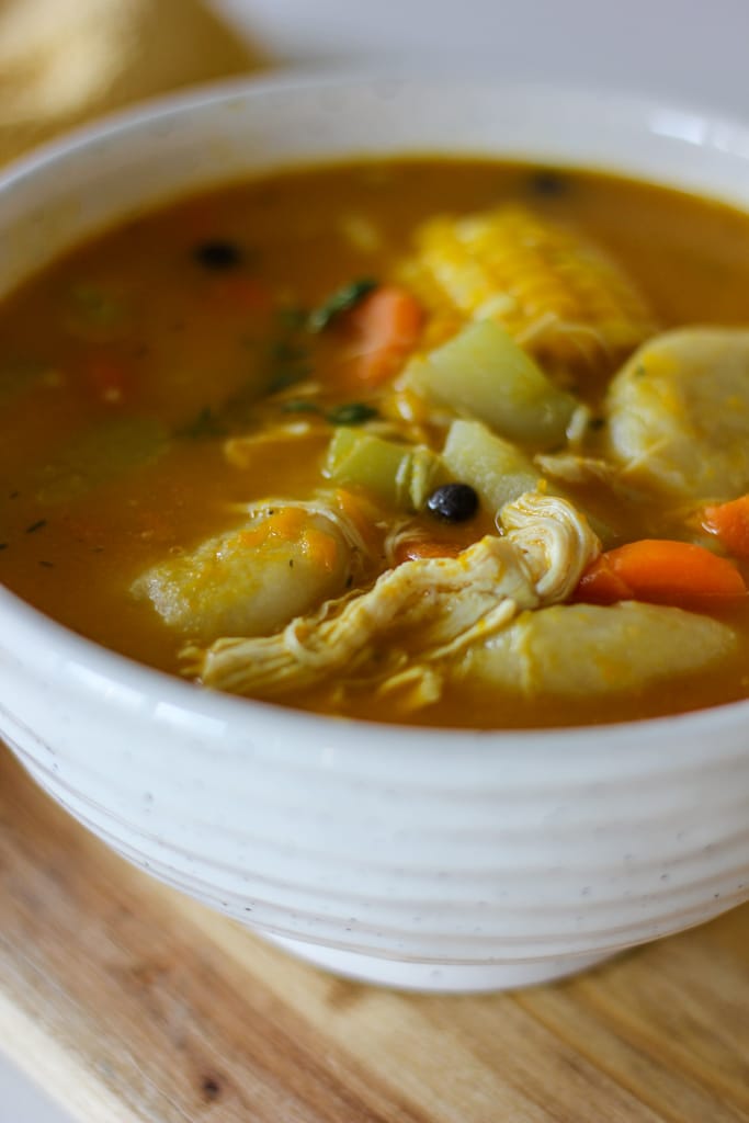 jamaican chicken soup in white bowl on wooden plank.