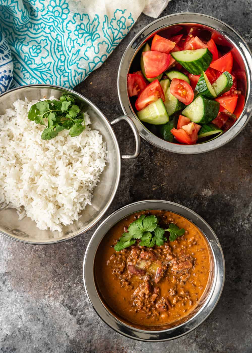 serving bowls of black dal, rice and cucumbers with tomatoes