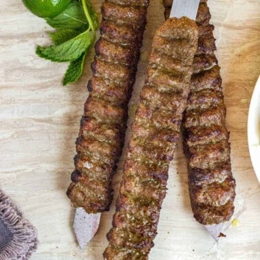 overhead of flat metal skewers with Koobideh babobs on a wooden table