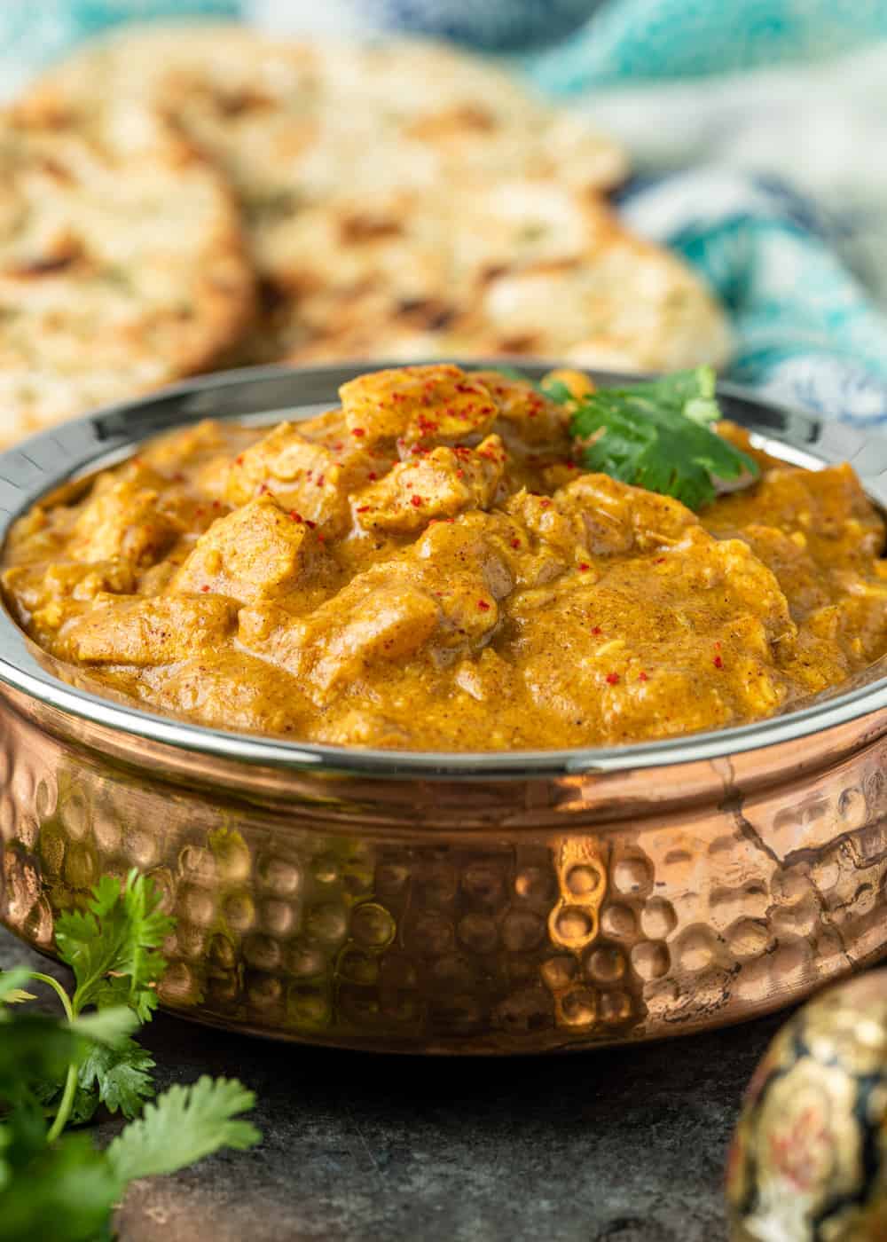 chicken korma in a copper serving bowl, garnished with paprika and fresh cilantro