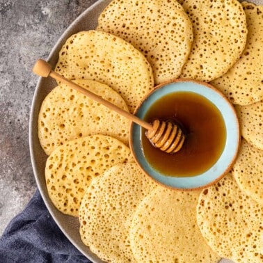 close up overhead image: platter of semolina pancakes arranged around a bowl of honey