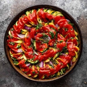 overhead image: Greek roasted vegetables on round platter topped with tomato sauce