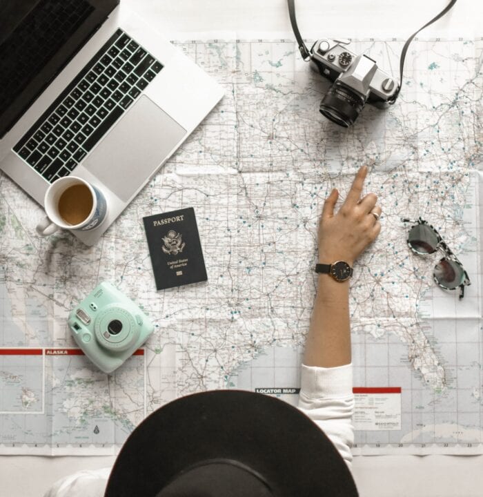 How to plan a road trip with Google Maps - woman pointing at a road map with a camera, passport, and laptop