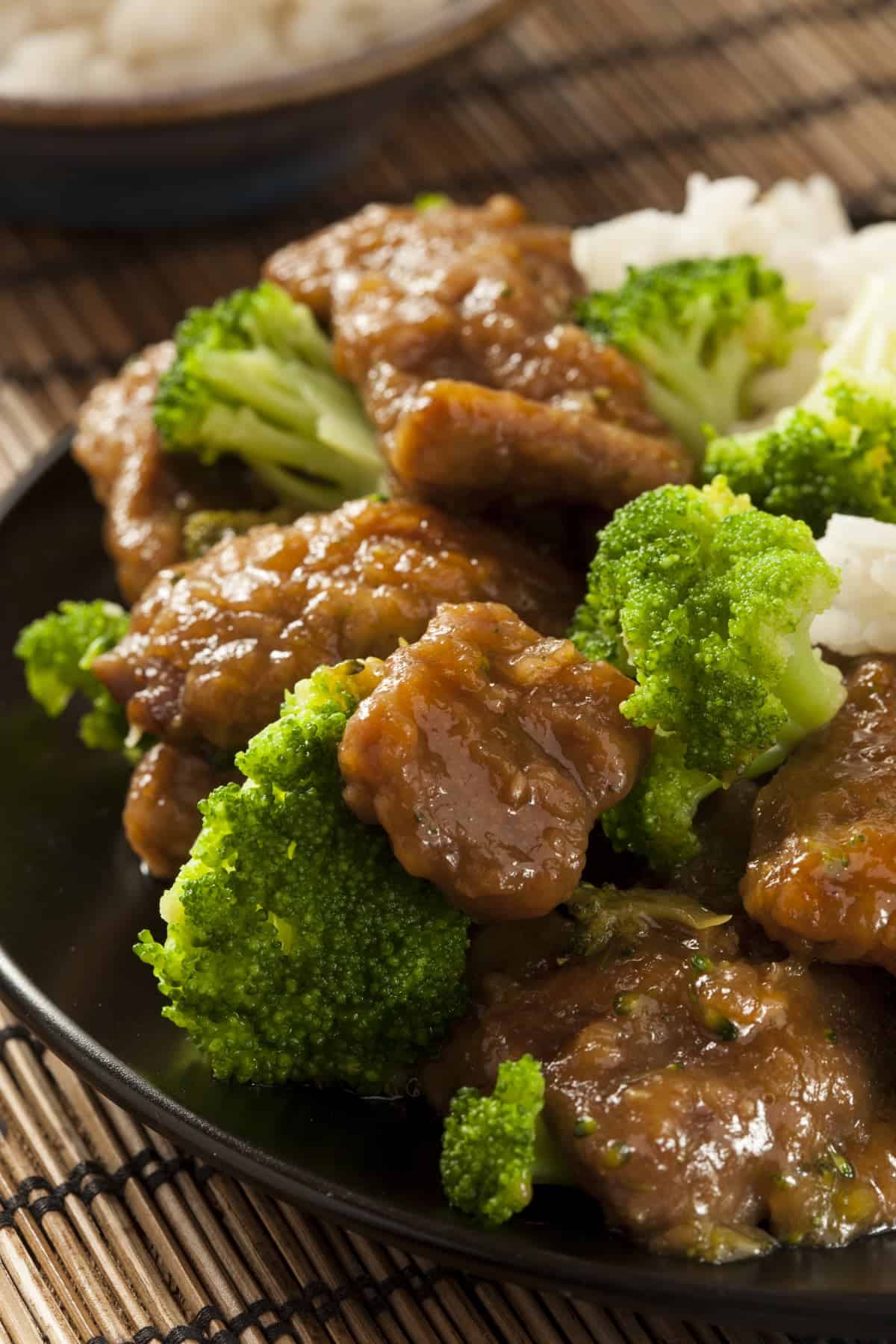 Beef with Broccoli and white rice on dark plate on bamboo mat.