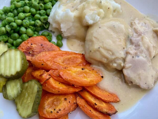 crock pot chicken cooked in creamy soup with peas, roasted carrots and pickles on white plate