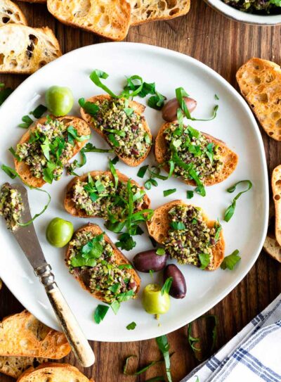 gray bowl full of green olive tapenade a topped with fresh parsley leaves.