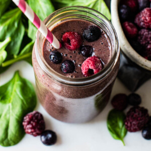 Overhead photo of a spinach berry smoothie topped with berries and surrounded by fresh spinach.