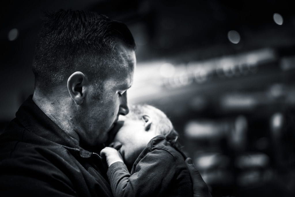 A man, face turned away from the camera, holds a sleeping baby. 