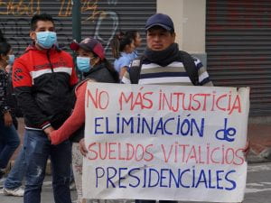 A man holding a protest sign with a few people to the left.