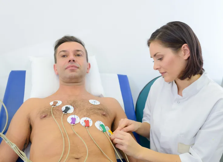 Female cardiovascular technician applies cardiogram electrodes on a male patient’s chest for an EKG