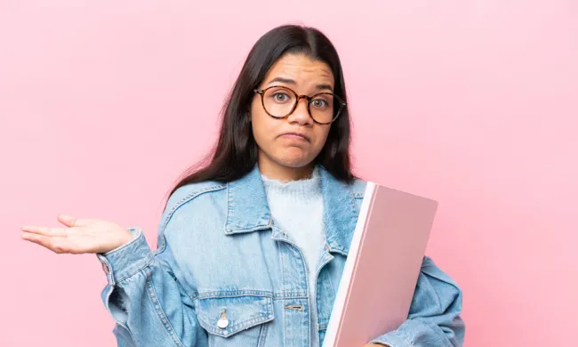 Young woman wearing blue jean jacket and carrying a notebook shrugs 