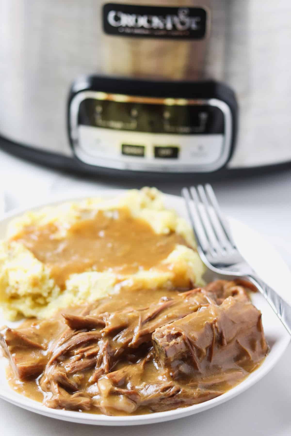 plate of pot roast and mashed potatoes with gravy with crock pot in background